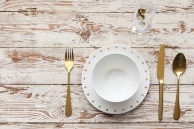 Beyaz ahşap arka planda altın çatal bıçak takımı olan zarif bir masa.