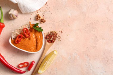 Bir kase lezzetli muhammara ve bej arka planda malzemeler.