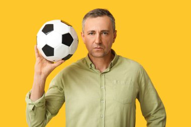 Sarı arka planda futbol topu olan yakışıklı olgun bir adam.
