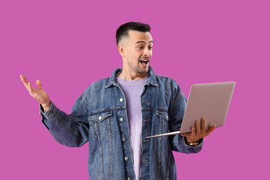 Mor arka planda dizüstü bilgisayarı olan şaşırmış genç bir adam.