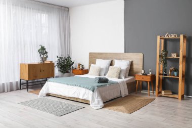 Yatak odasının içinde ahşap yatak, ev bitkileri ve komodinin yanında çalar saat var.