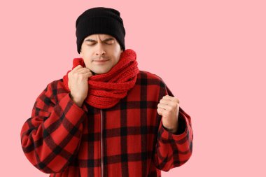 Pembe arka planda kışın giyinmiş donmuş genç adam.