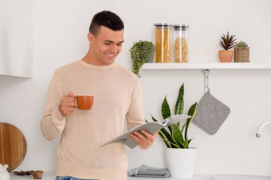 Evdeki mutfakta bir fincan kahve okuyan yakışıklı genç adam.