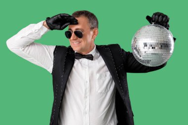 Yeşil arka planda disko topu olan takım elbiseli havalı olgun bir adam.