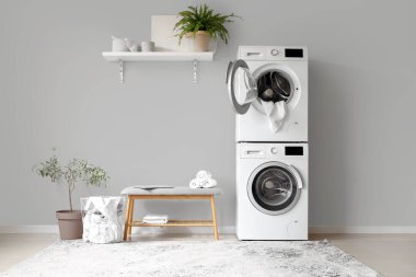 Çamaşır makinesi ve gri banklı modern çamaşır odasının içi.