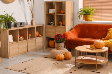 İçinde kahverengi kanepe, ahşap mobilya ve balkabağı olan rahat bir oturma odası.