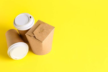 Paketlenmiş kağıt bardaklar ve sarı arka plandaki kutu.