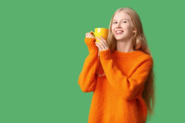 Yeşil arka planda bir fincan çayı olan güzel, genç ve mutlu bir kadın.