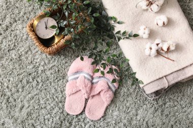 Çalar saati olan yumuşak terlikler, bitki, pamuk çiçekler ve yeşil halıda ekose, üst manzara.