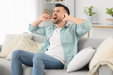 Evdeki gürültücü komşular yüzünden kulakları tıkalı genç bir adam.