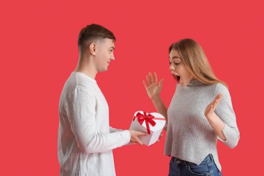 Kırmızı arka planda hediye kutusu olan sevimli bir çift. Sevgililer Günü kutlaması