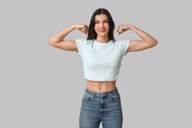 Young woman flexing muscles on grey background. Feminism concept