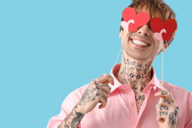 Funny young man with paper hearts on blue background. Valentine's day celebration