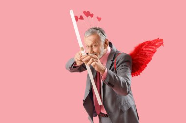 Aşk tanrısı gibi giyinmiş olgun bir adam pembe arka planda ok atıyor. Sevgililer Günü kutlaması