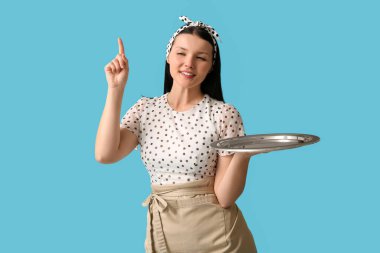 Tepsisi mavi arka planda bir şeyi gösteren güzel bir garson kız.