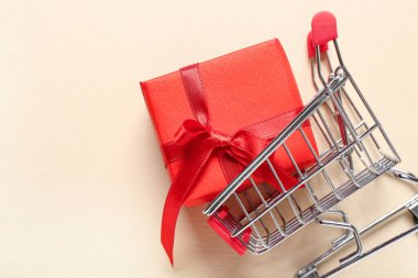 Bej arka planda hediye kutusu olan küçük bir alışveriş arabası. Sevgililer Günü kutlaması