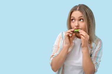 Güzel genç bir kadın mavi arka planda yeşil badem kurabiyesi yiyor.