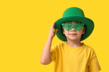 Leprikon şapkalı ve sarı arka planda yonca şeklinde dekoratif gözlüklü şirin bir çocuk. Aziz Patrick Günü kutlaması