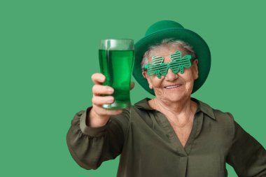Yeşil arka planda bir bardak birası olan cüce şapkalı ve dekoratif gözlüklü yaşlı kadın. Aziz Patrick Günü kutlaması