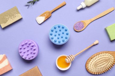 Saç derisi masaj aletleri, şampuan çubukları, bir kase bal ve mor arka planda deniz tuzu.