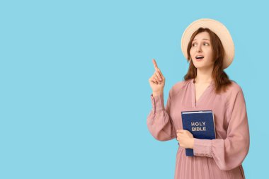İncil 'i olan dindar genç bir kadın mavi arka plandaki bir şeyi işaret ediyor.