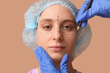 Plastik cerrah, kadın yüzüne yakın plan kahverengi arka plan üzerinde izler uyguluyor. Blepharoplasty konsepti