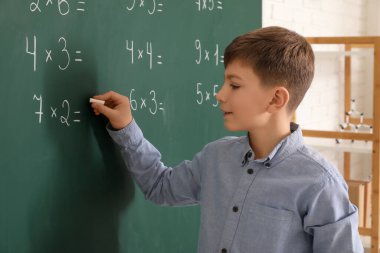 Sınıfta ders sırasında tahtaya yazı yazan sevimli çocuk.