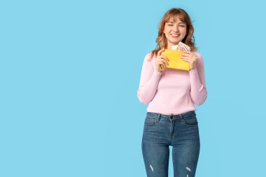 Sarı cüzdanı olan, mavi arka planda parası olan güzel bir kadın.