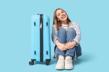 Arka planda mavi bavulu olan mutlu genç bir kadın.