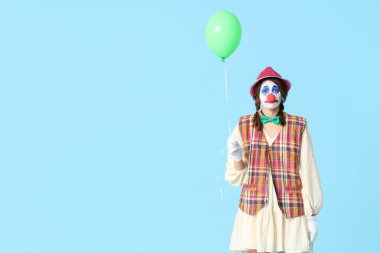 Mavi arka planda balonu olan üzgün bir palyaço gibi giyinmiş genç bir kadın. 1 Nisan şakası