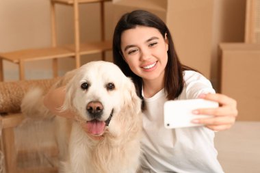 Genç mutlu bir kadın ve kutuları olan şirin Labrador köpeği taşınma gününde selfie çekiyorlar.