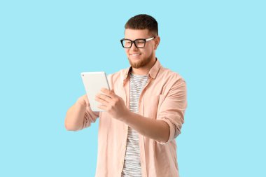 Mavi arka planda tablet bilgisayar kullanan gözlüklü genç adam.