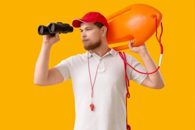 Kurtarma şamandırası ve sarı arka planda dürbünü olan genç bir erkek cankurtaran.