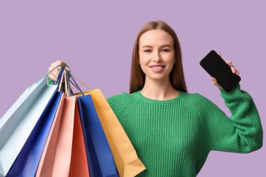 Leylak arka planında alışveriş çantaları ve cep telefonu olan genç bir kadın.