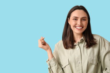 Gülümseyen genç bir kadın mavi arka planda kalp hareketi gösteriyor.