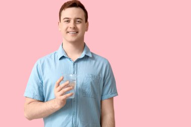 Handsome young man with glass of clean water on pink background