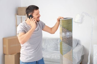 Halısı sarılı genç adam taşınma gününde cep telefonuyla konuşuyor.