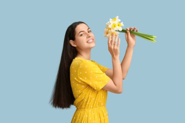 Mavi arka planda bir buket nergis çiçeğiyle güzel genç bir kadın.