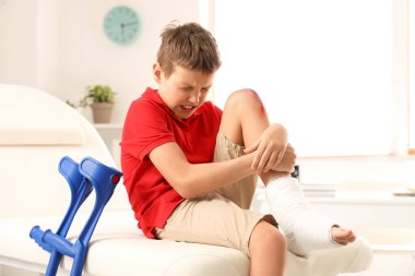 Little boy with wounded knee sitting on couch in clinic