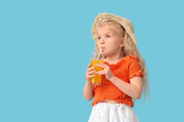 Sevimli küçük kız mavi arka planda portakal suyu içiyor.