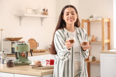 Mutfakta bir fincan taze kahveyle güzel, genç, mutlu bir kadın.