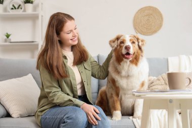 Evdeki kanepede oturan sevimli Avustralya çoban köpeği olan genç bir kadın.
