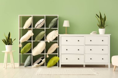 Yastıklı ve çekmeceli raf ünitesi yeşil duvarın yanında.