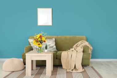 Oturma odasındaki sehpanın üzerindeki vazoda ekose ve yabani çiçeklerle dolu rahat bir kanepe.