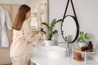 Banyoda elinde bir şişe kozmetik ürünü olan genç bir kadın.