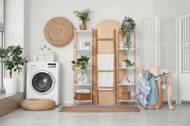 Çamaşır sepetli, çamaşır makineli ve raflı çamaşır odasının içi.