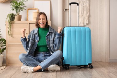 Koridordaki kapının yanında bavullu mutlu bayan turist.