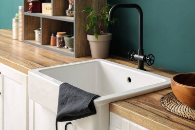 Beyaz seramik lavabo ve raf ünitesi mutfaktaki koyu mavi duvarın yanındaki ahşap tezgahın üzerinde.