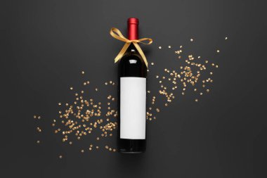 Siyah arka planda yay ve konfeti olan bir şişe şarap.