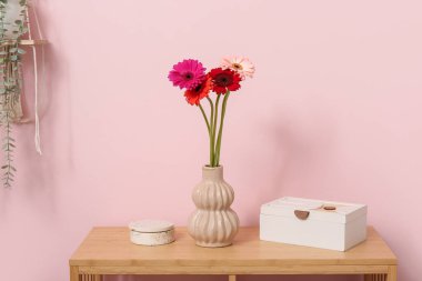 İçinde Gerbera çiçekleri olan vazolar ve raf ünitesinde pembe duvarın yanında duran kutular. Yakın çekim.